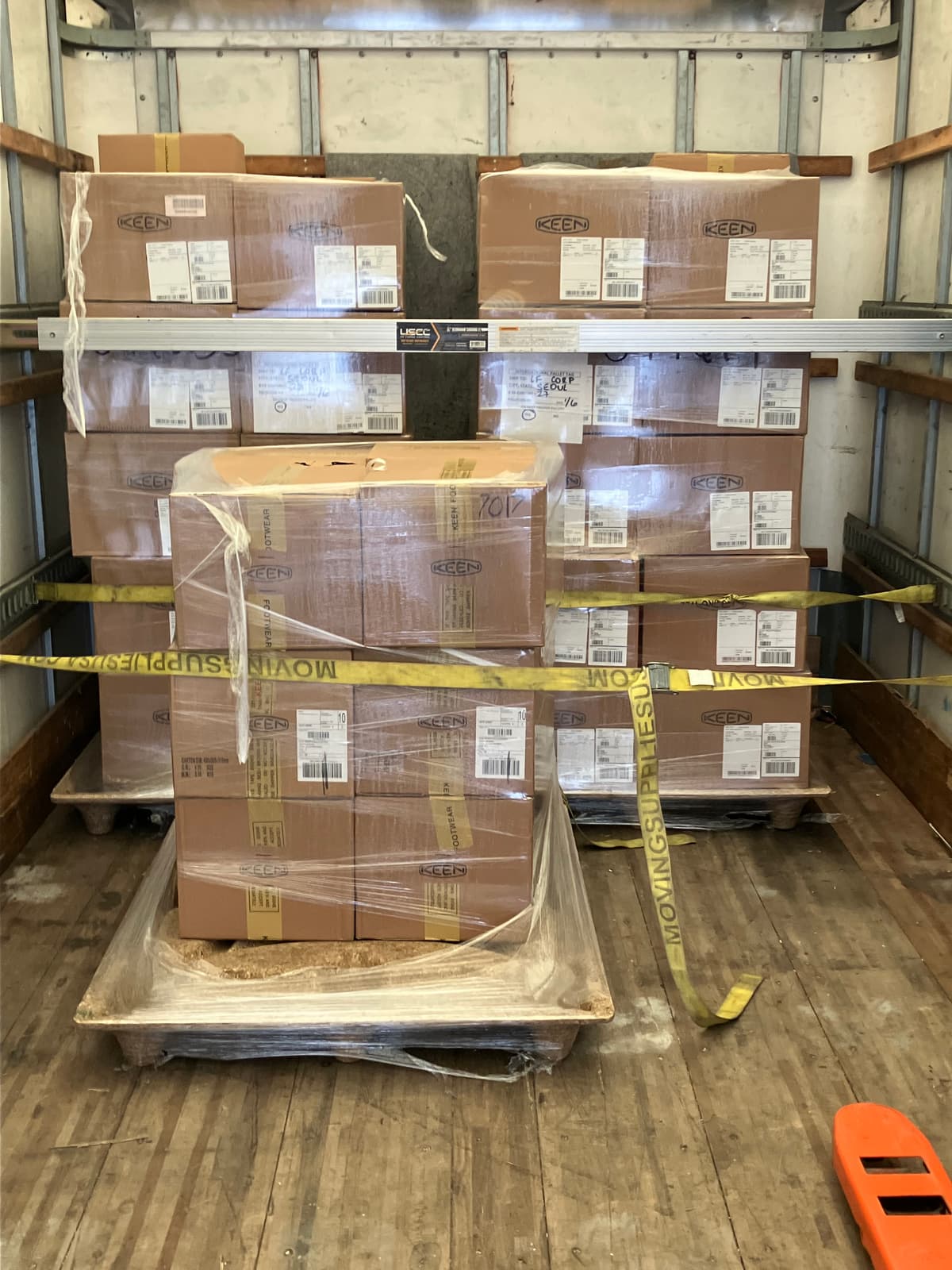 Shrink-wrapped pallets of boxed freight strapped and load-barred inside a wood-floor box truck.