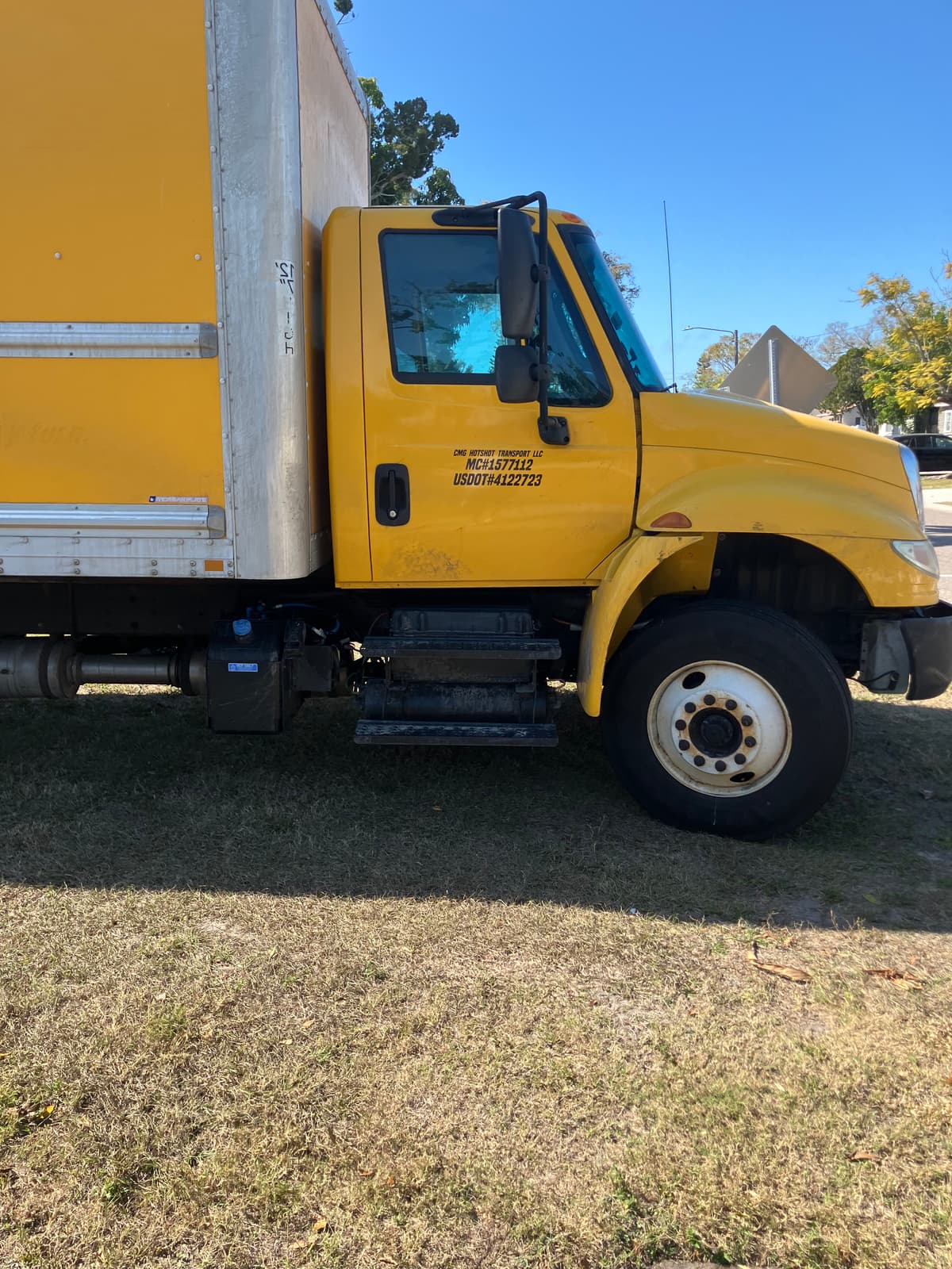 CMG's yellow 26ft box truck parked on grass, company name and MC and USDOT numbers lettered on the cab door.