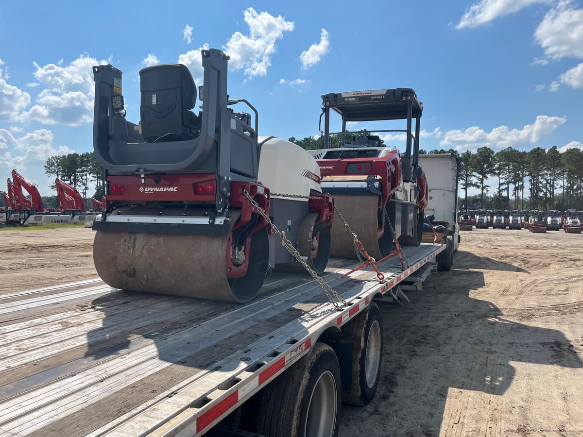 Two asphalt rollers chained down on a flatbed trailer in an equipment yard.
